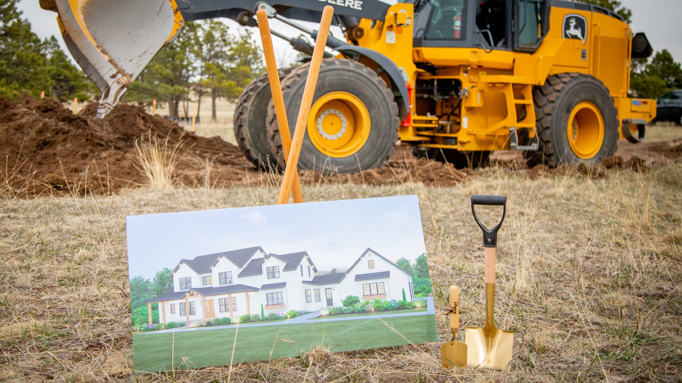 Gold shovels and a rendering of the home beside the excavator on groundbreaking day